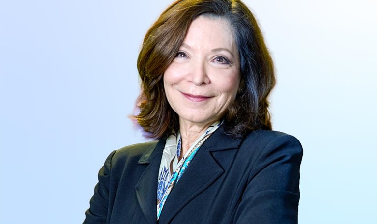 Leslie Davis wearing a blue jacket, arms folded, warmly smiling.