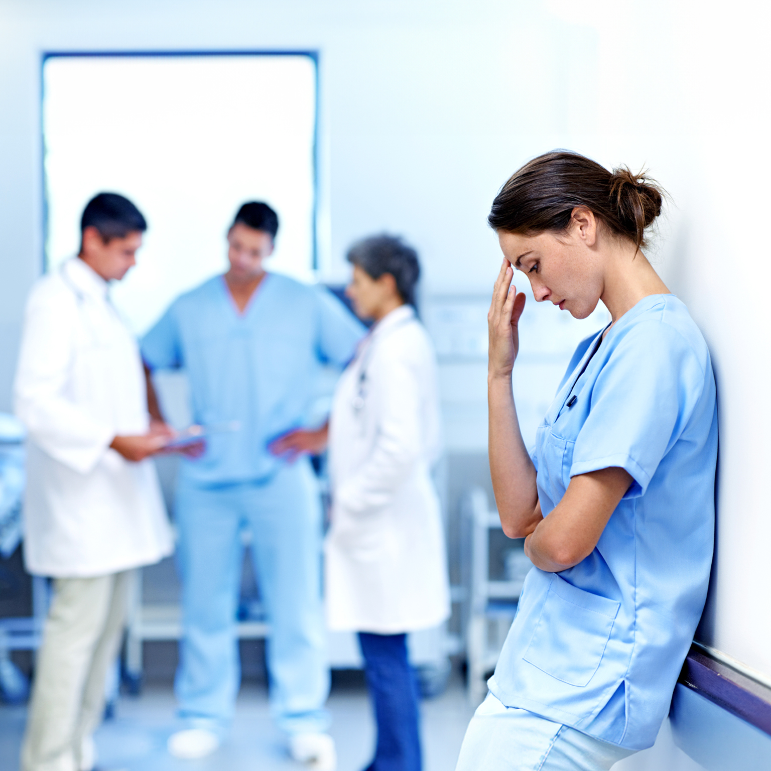 It's been a long shift. Shot of an exhausted doctor leaning against a wall with colleagues in the background. - stock photo
