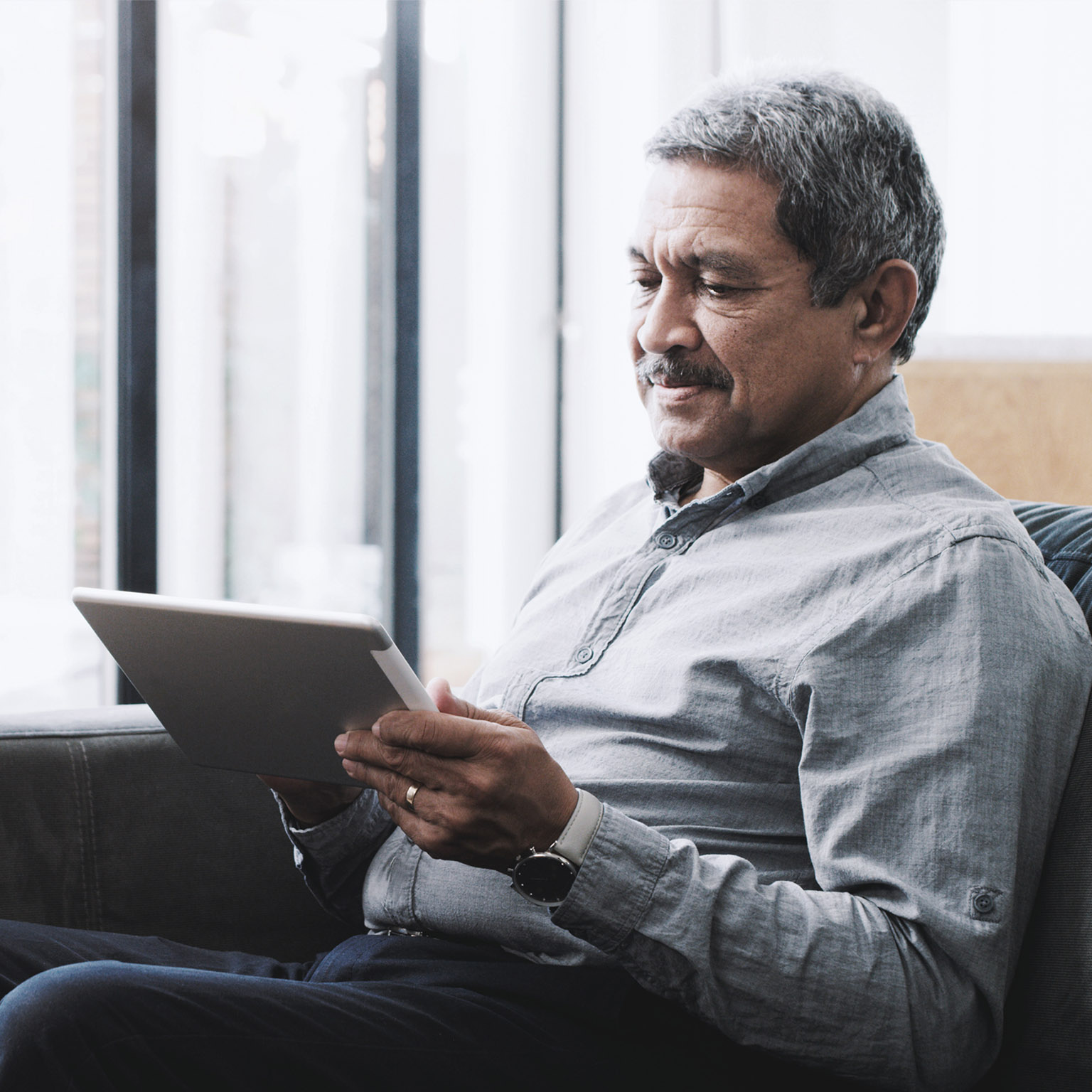 Senior man using a digital tablet on the sofa at home.