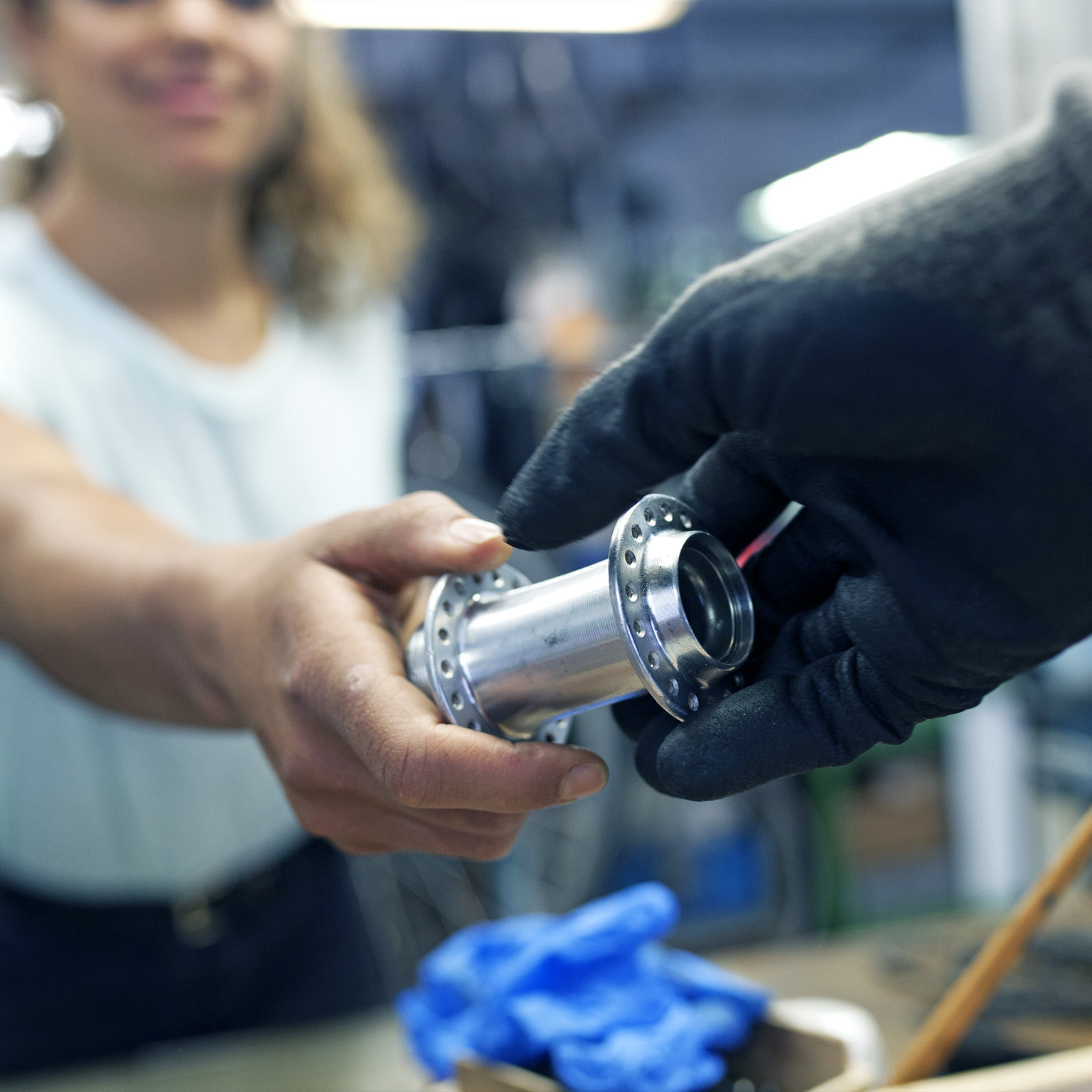 A close up of a technician handing her colleague a bike part while working together in a bicycle workshop