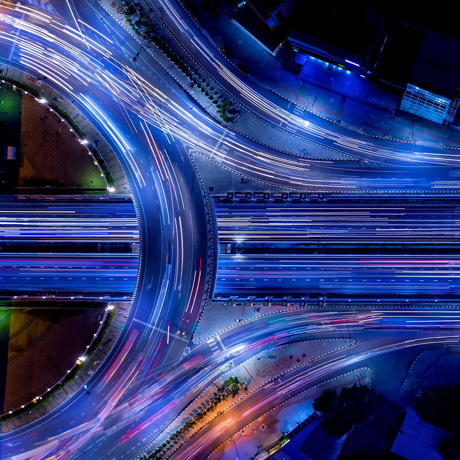 Aerial night view of a highway interchange with vibrant blue-toned long-exposure light trails from moving traffic.