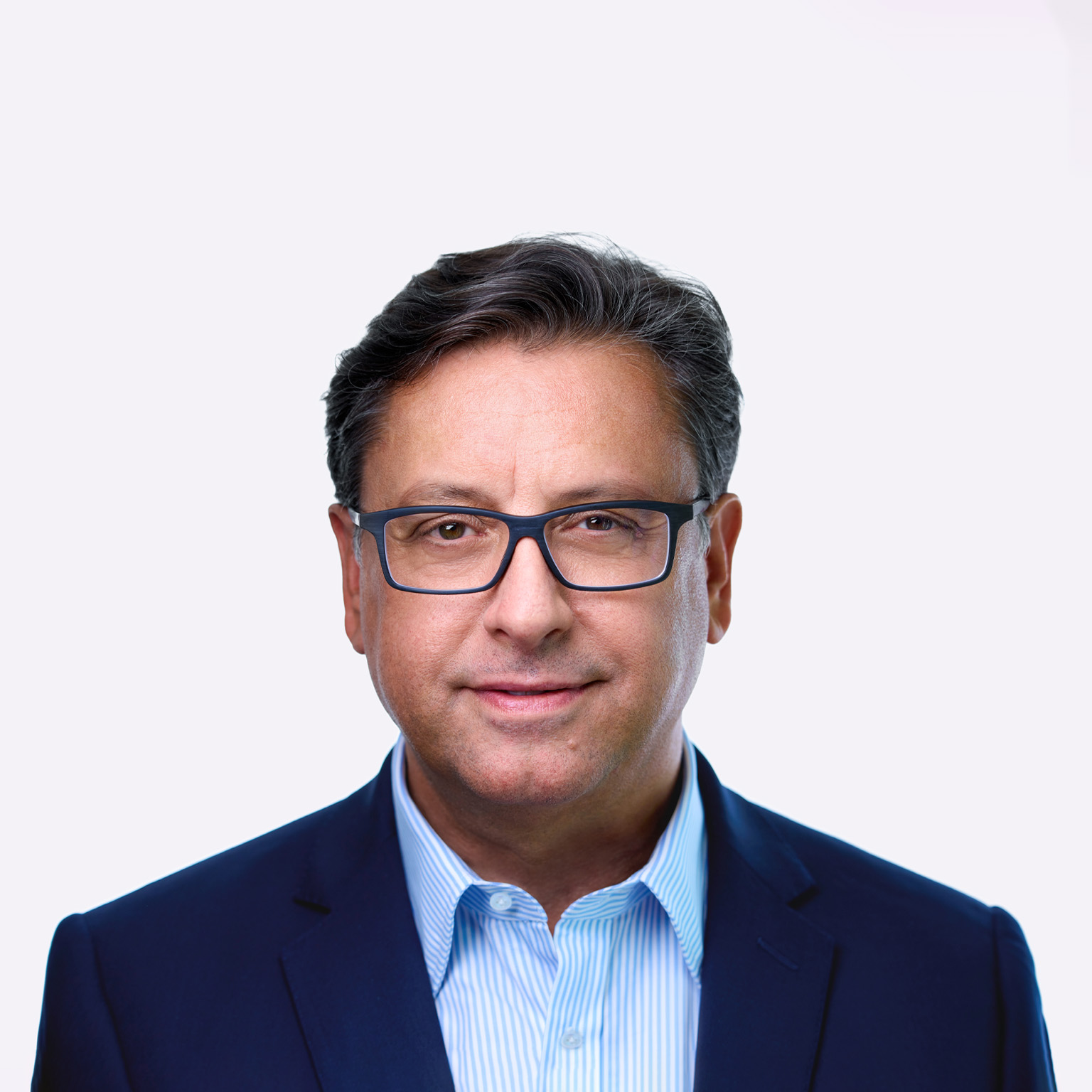 A man named Paul Hudson, sporting dark hair and glasses, can be seen in a slight smile as he faces the camera. He is dressed in a blue suit jacket and a striped blue shirt.