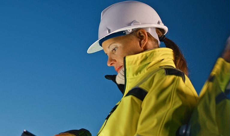 Female worker in protective workwear using tablet PC while standing by car at oil industry against sky