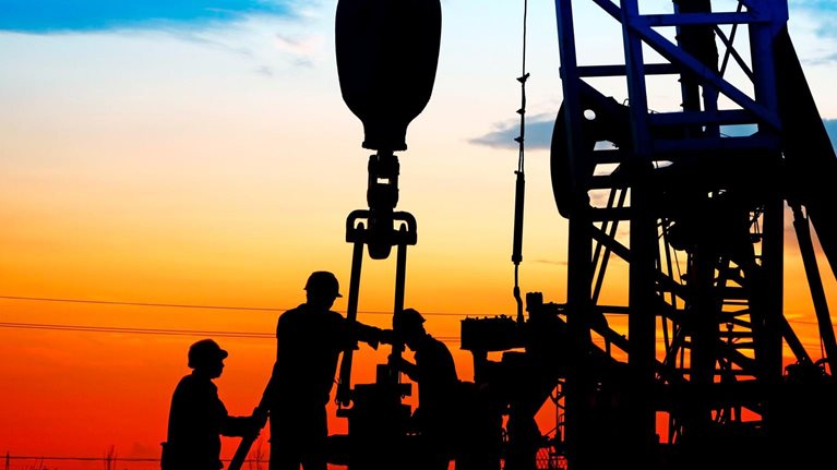 Silhouetted workers operating an oil drilling rig, against a vivid sunset sky with gradients of orange, red, and blue.