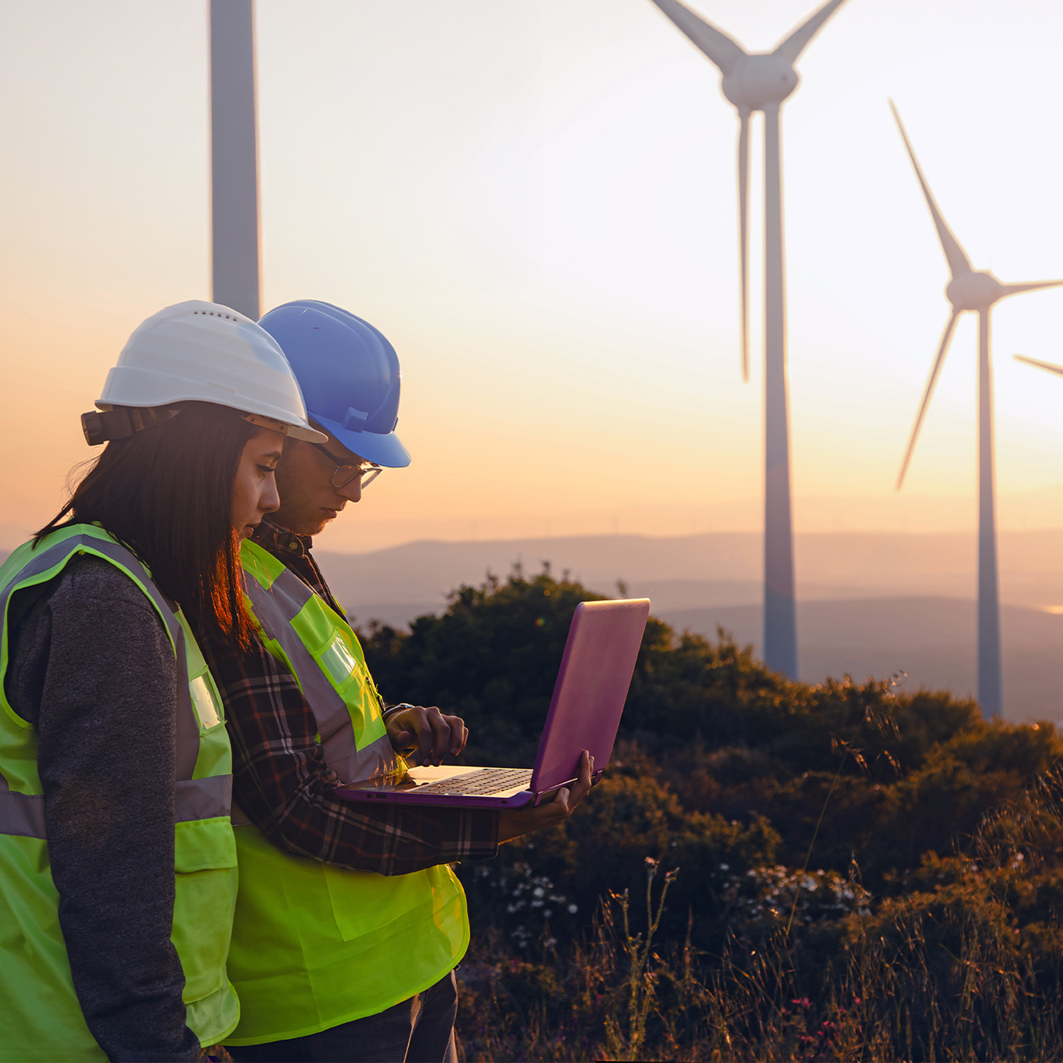 Engineers with Safety Helmets and Vests Using Laptop at Wind Farm During Sunset, Highlighting Renewable Energy, Sustainability, and Green Technology Innovation