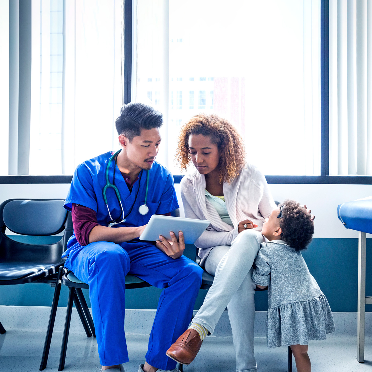 Male nurse showing digital tablet to mother with toddler in hospital