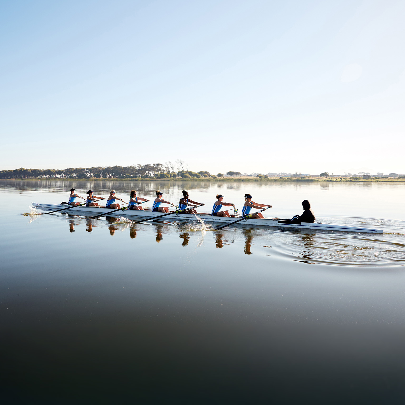 Female rowing team rowing scull on tranquil lake