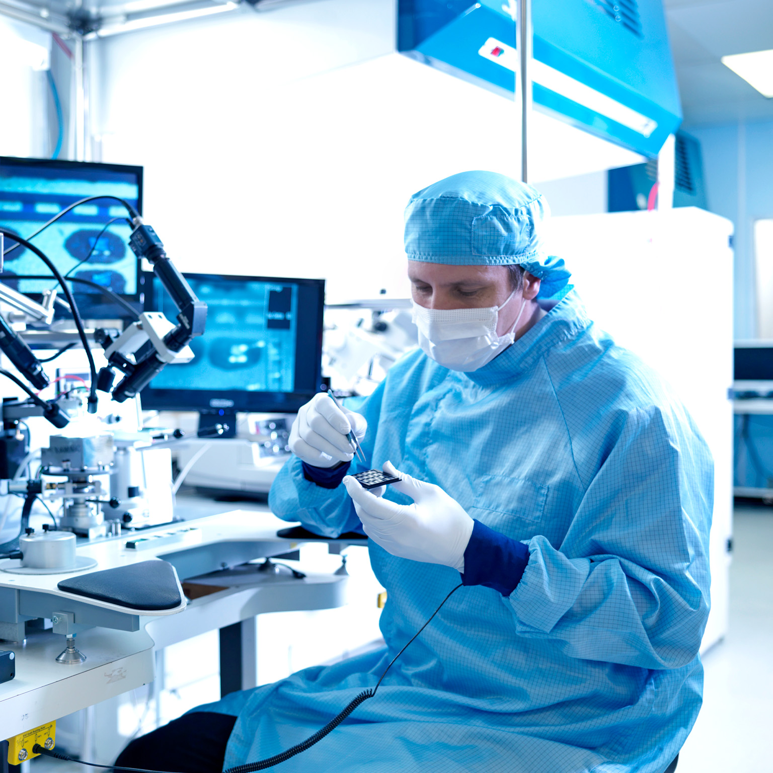 Electronics workers selecting chips at workstation in clean room laboratory