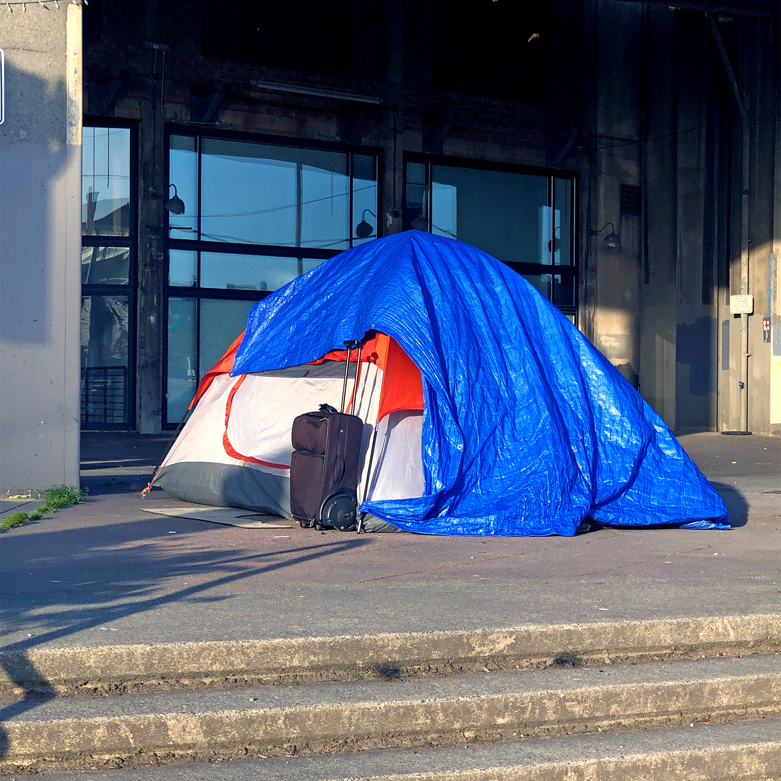 Tarped tent and suitcase on a city sidewalk