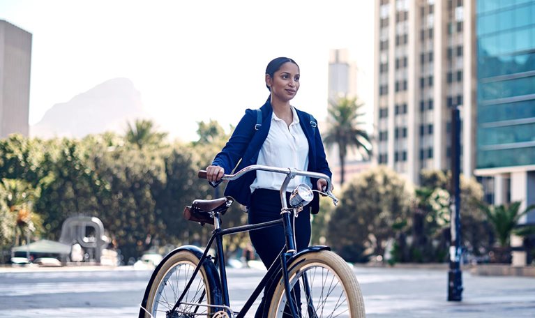 A young South African businesswoman walking her bicycle through a modern downtown. Table mountain is seen in the distance.
