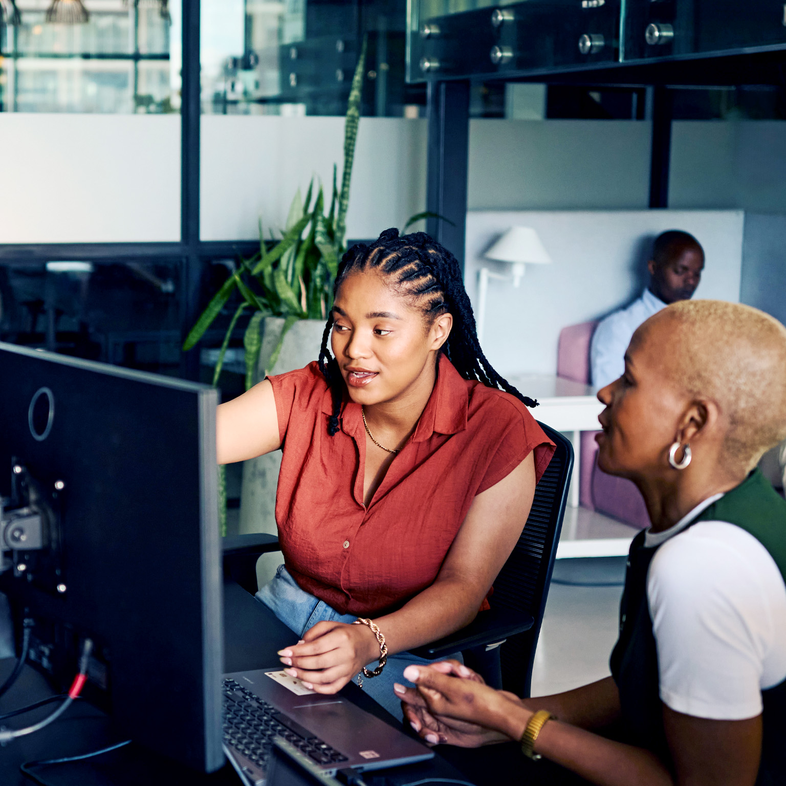 Two women collaborating closely at a computer, intensely focused on the screen. The one woman gestures towards the monitor, suggesting an learning or problem-solving session.