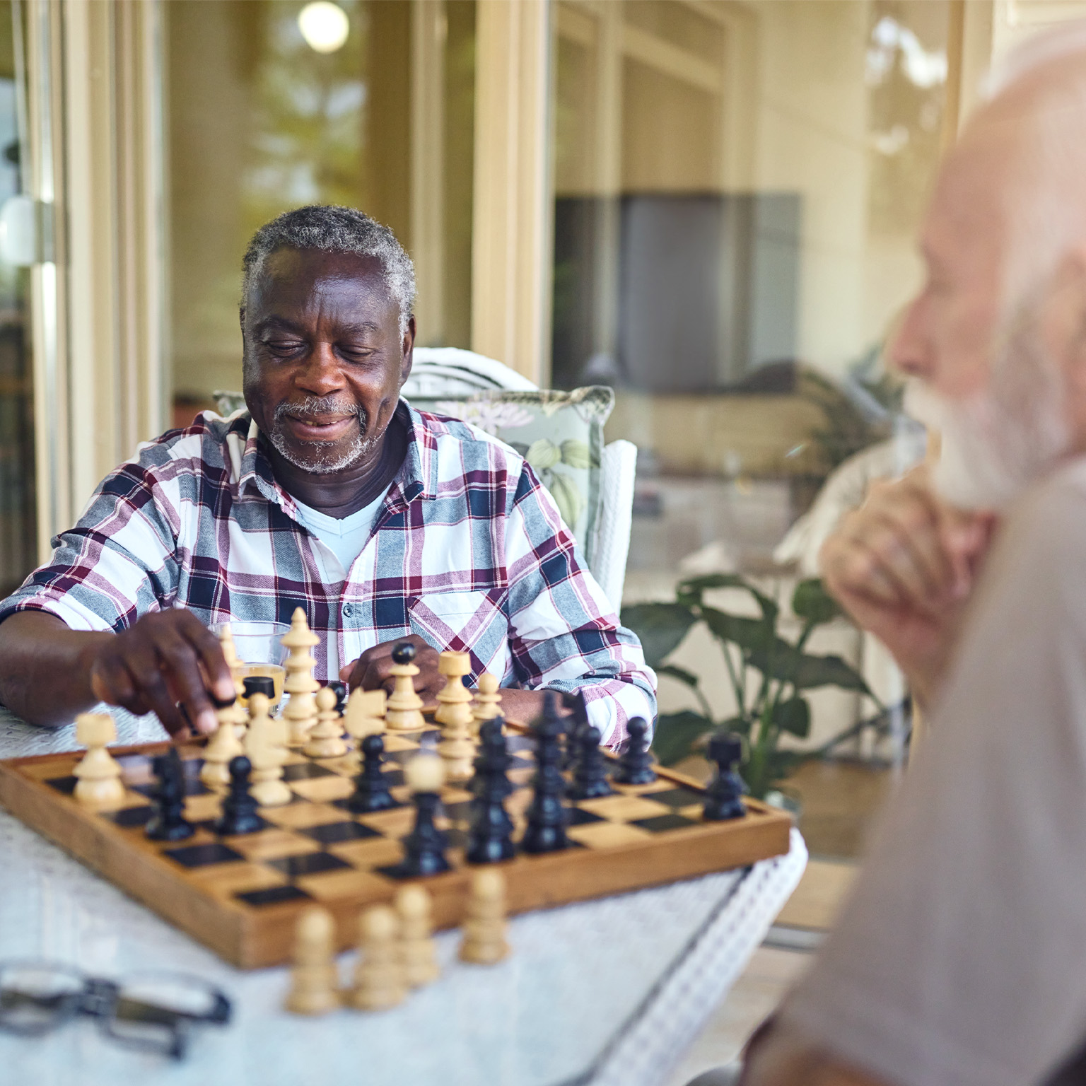 Two elderly gentlemen playing chess on a warmly lit patio in a senior living facility.