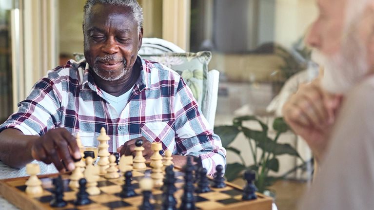 Two elderly gentlemen playing chess on a warmly lit patio in a senior living facility.