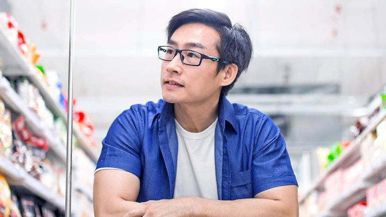 An Asia mature man pushes shopping cart and browses for products in groceries shop