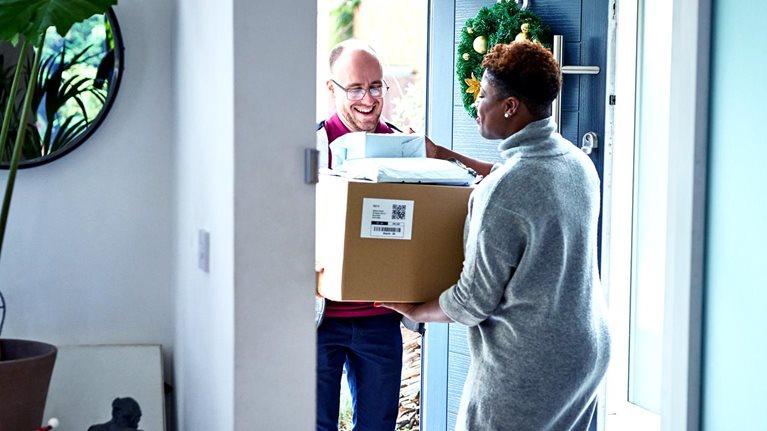 Delivery man handing over cardboard box to female customer during holiday season.
