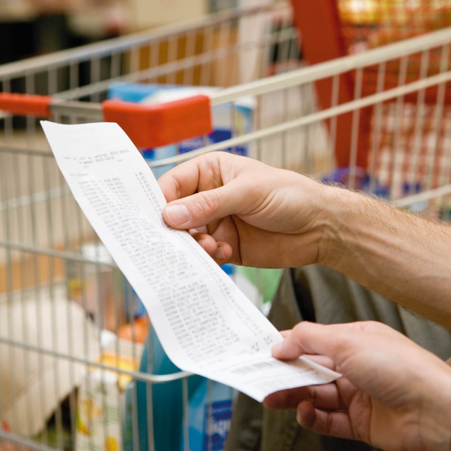 photo of hand holding grocery receipt in front of shopping cart