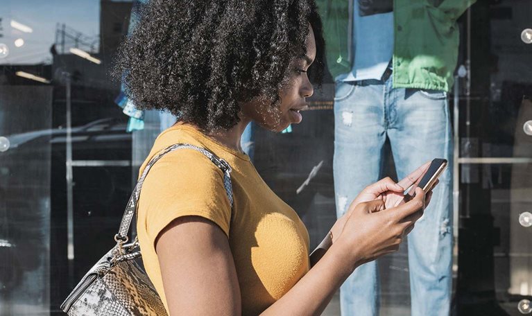 Young woman looking at phone outside shop window