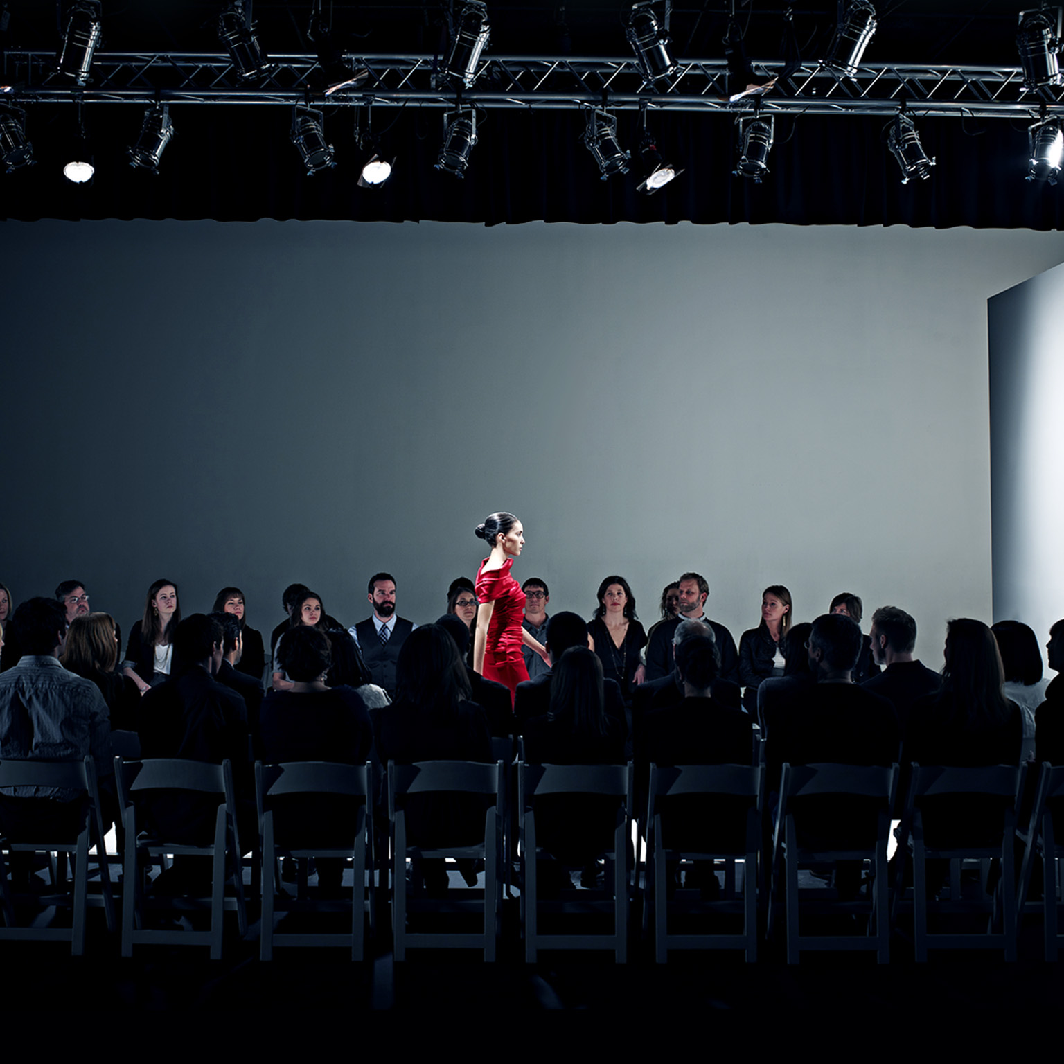 Female model walking on catwalk in front of crowd at fashion show.