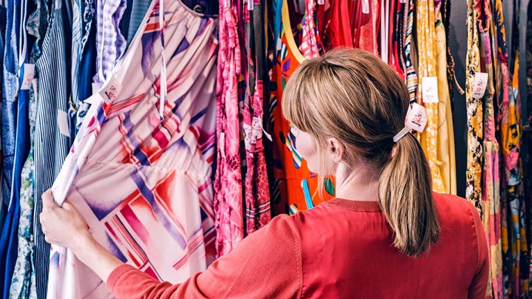 Woman looking at dress hanging on rack while standing in store