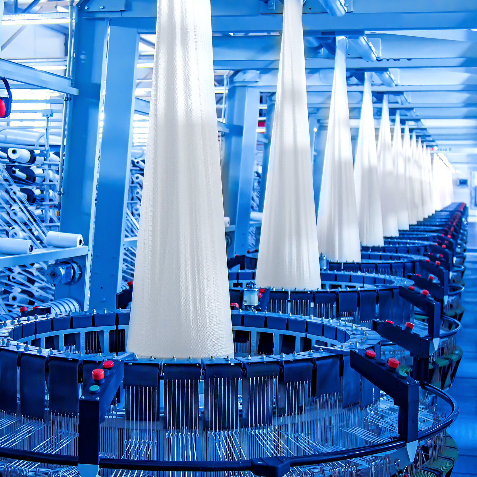 Image of a factory producing white flat yarn in multiple large loom machines.
