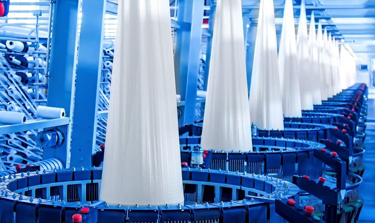 Image of a factory producing white flat yarn in multiple large loom machines.