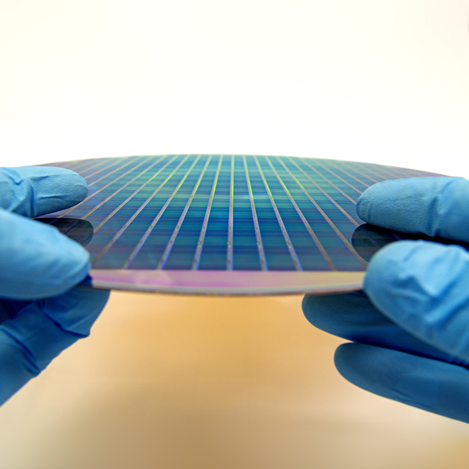 Image of gloved hands holding a patterned 300 mm silicon wafer.