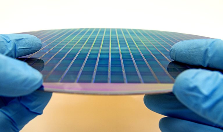 Image of gloved hands holding a patterned 300 mm silicon wafer.