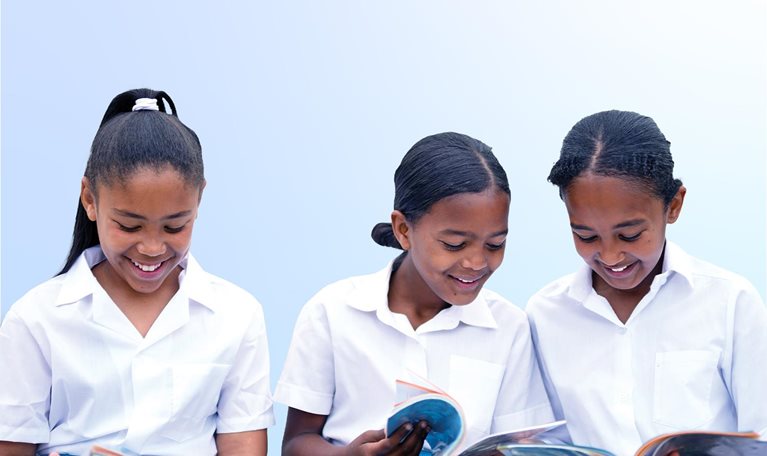 Schoolgirls looking through textbooks in school yard together