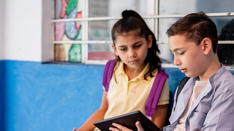 Child student friends talking and using digital tablet at school