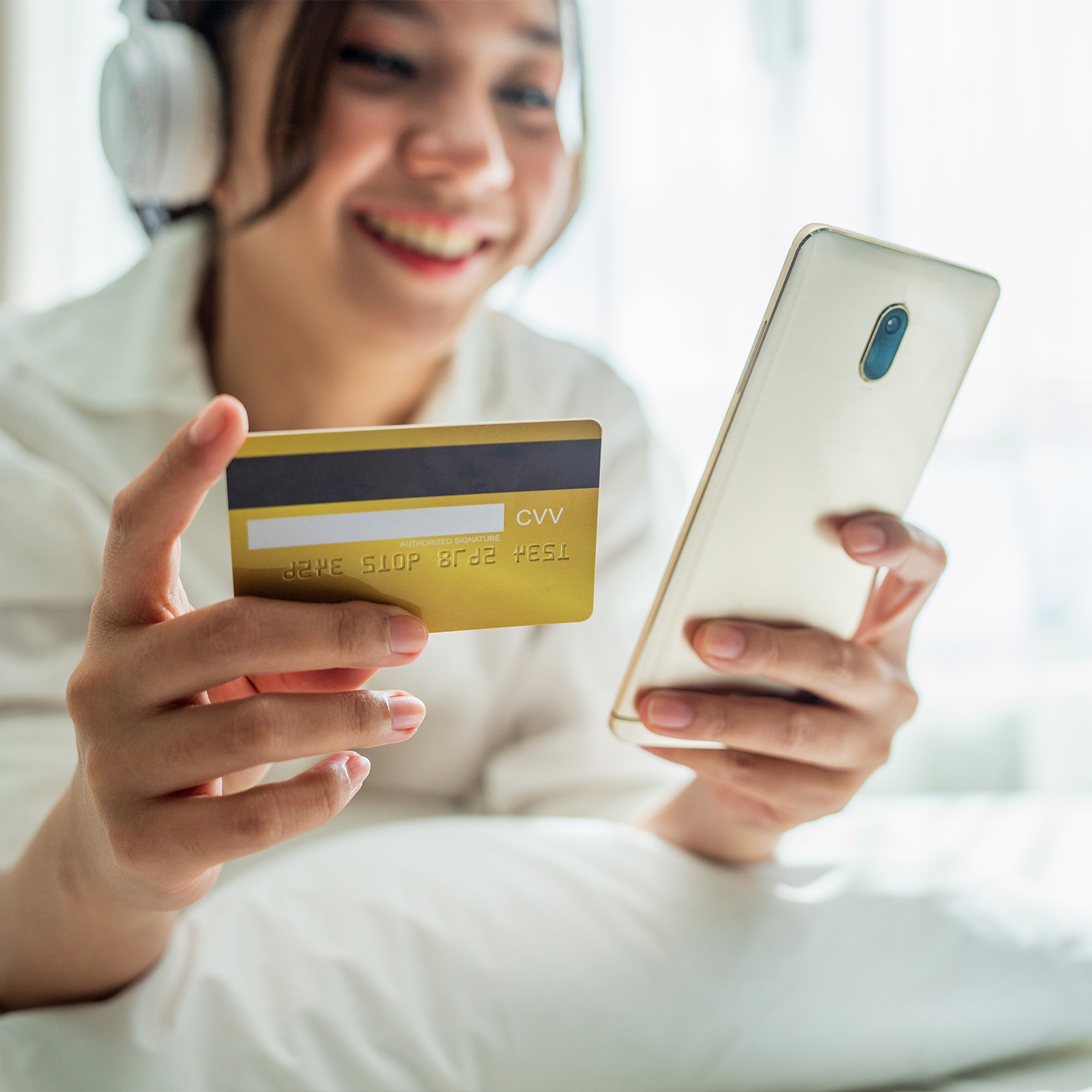 Happy smiling asian woman with white pajamas lay down on fluffy comfort bed use credit card online shopping successful payment on mobile phone in morning on bedroom at home. - stock photo
