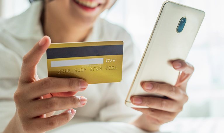 Happy smiling asian woman with white pajamas lay down on fluffy comfort bed use credit card online shopping successful payment on mobile phone in morning on bedroom at home. - stock photo