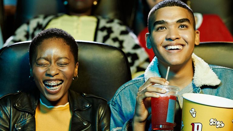 Cheerful young friends watching movie in theater.