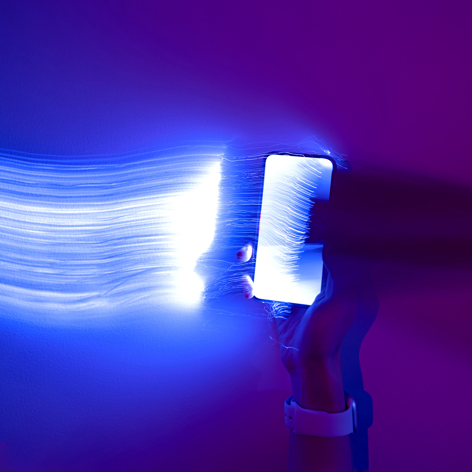Close-up photo of a hand holding a mobile phone with light streaks trailing out of it.