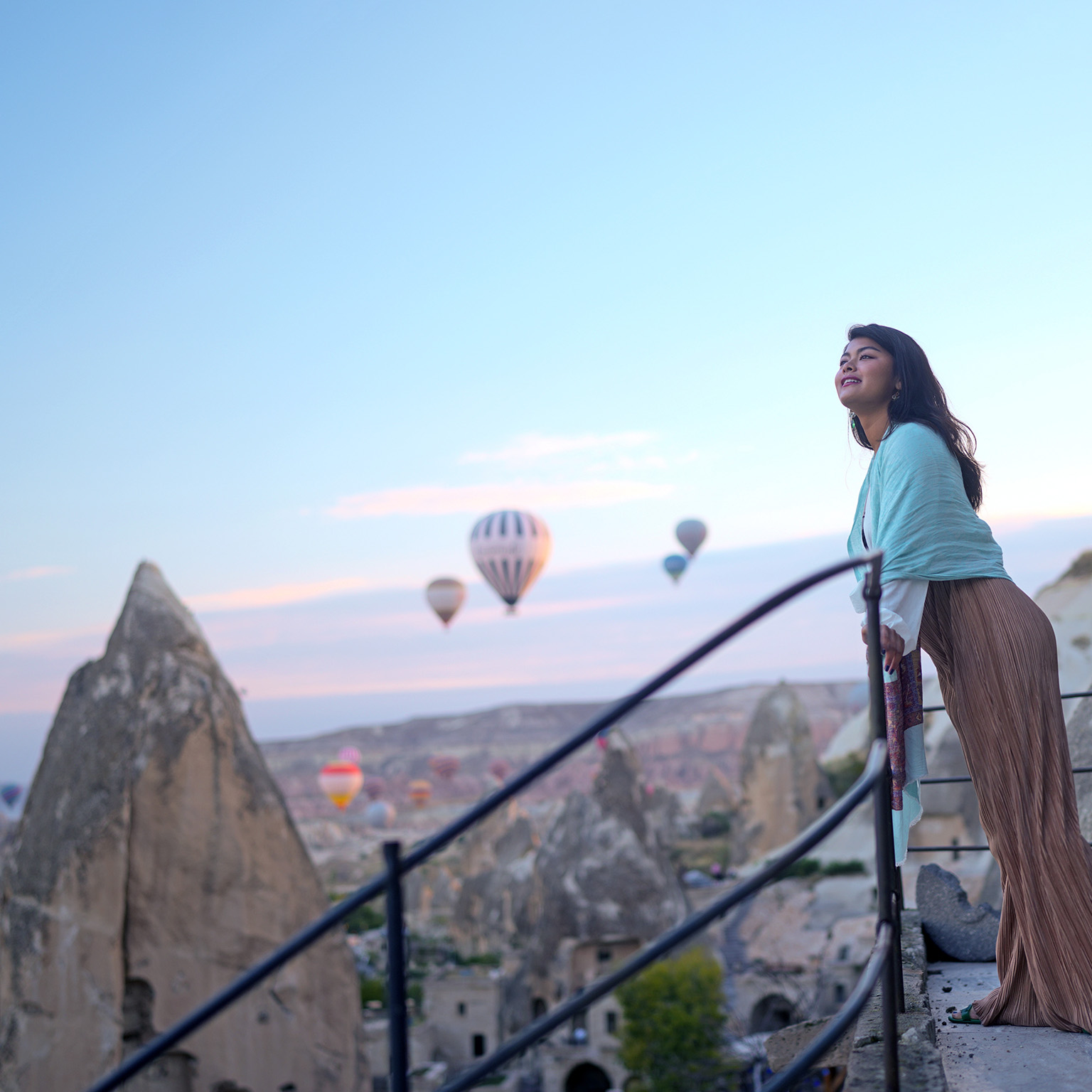 Portrait of young female tourist watching hot air balloons from a balcony on a cliff