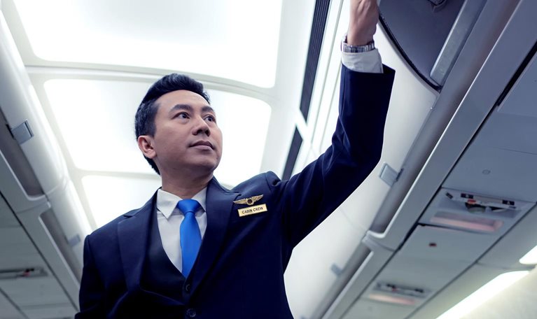 Image of a flight attendant closing overhead bins on an empty plane.