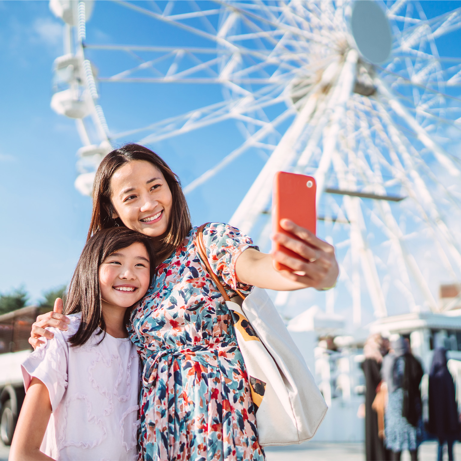 Mom and daughter taking selfie against a ferris wheel when enjoying spending time together in theme park - stock photo
