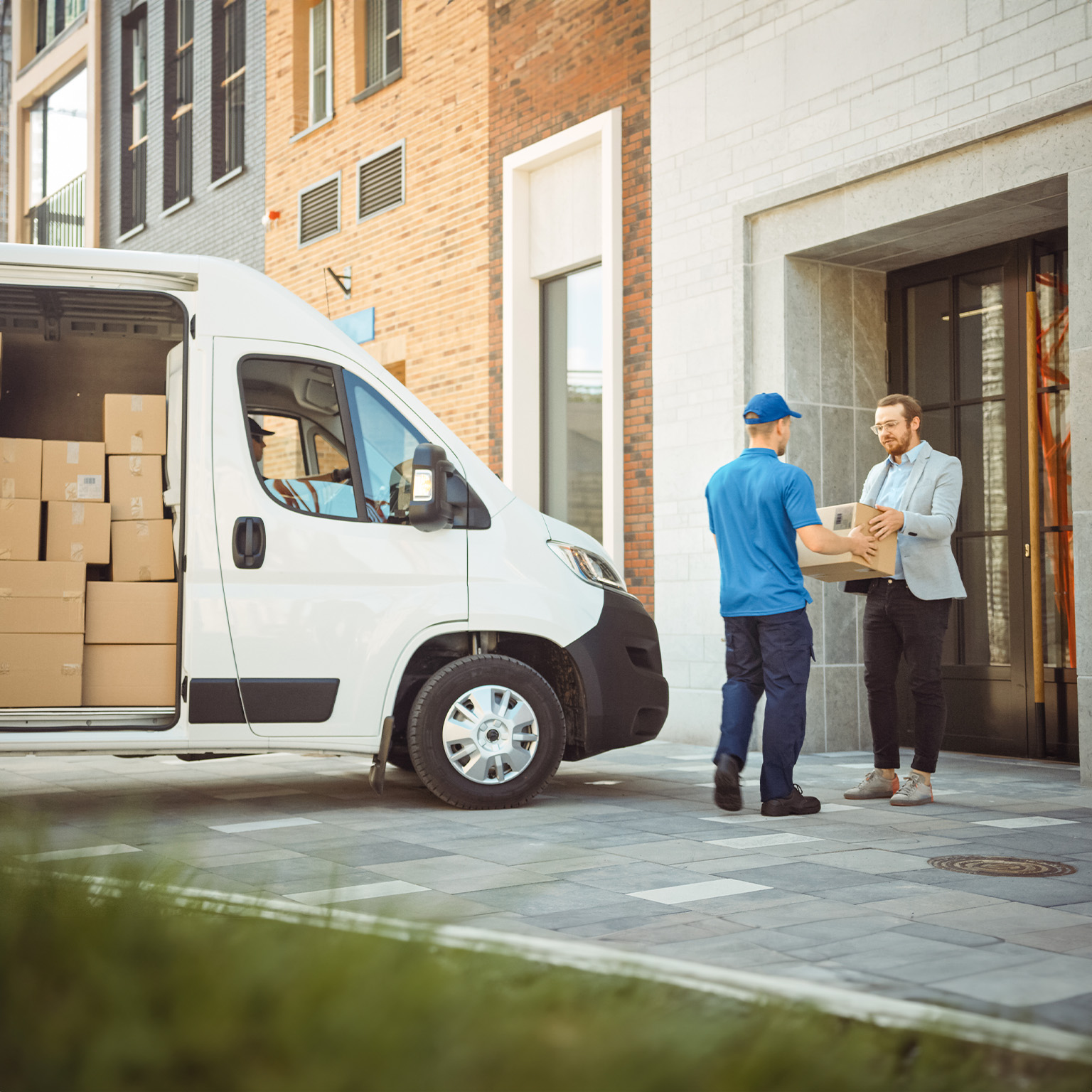 In stylish modern urban office area courier delivers cardboard box parcel to a man - stock photo