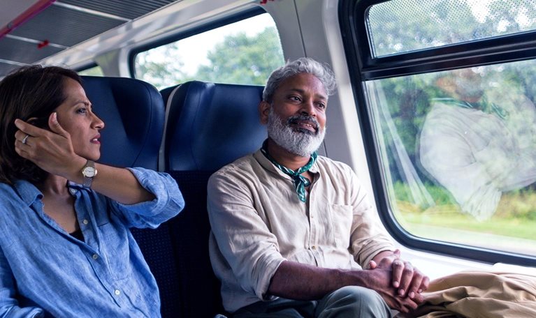 A mature Indian tourist couple riding in a commuter train in Lithuania, talking, having fun, and looking out the window.