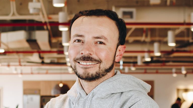 Portrait of a smiling Andres Melonn wearing a gray hoodie in a modern office.