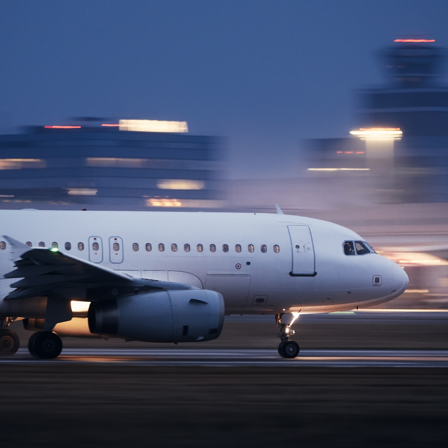 Image of an airplane taking off at night with blurred lit buildings in the background.