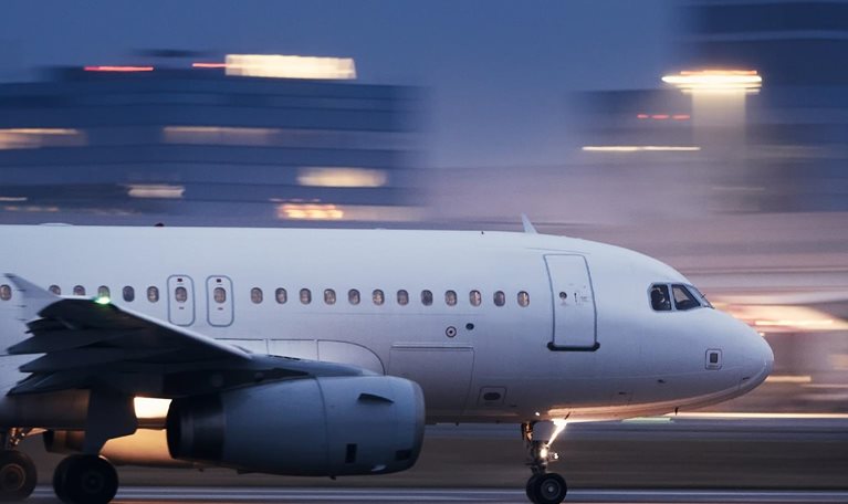 Image of an airplane taking off at night with blurred lit buildings in the background.