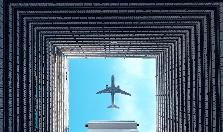 Airplane flying overhead, viewed through the open center of a high-rise building courtyard.