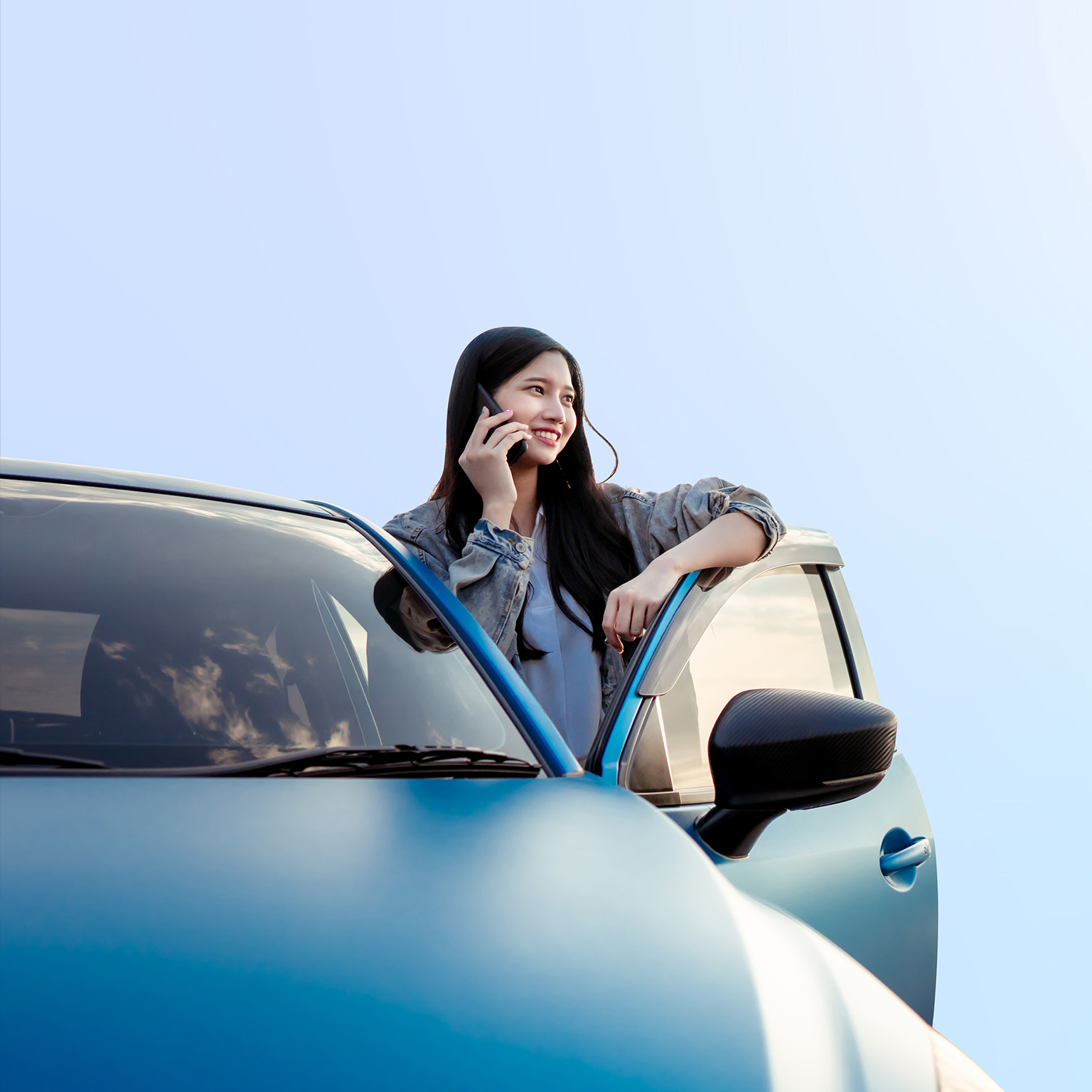 This image shows a person leaning against a blue car while talking on a phone.