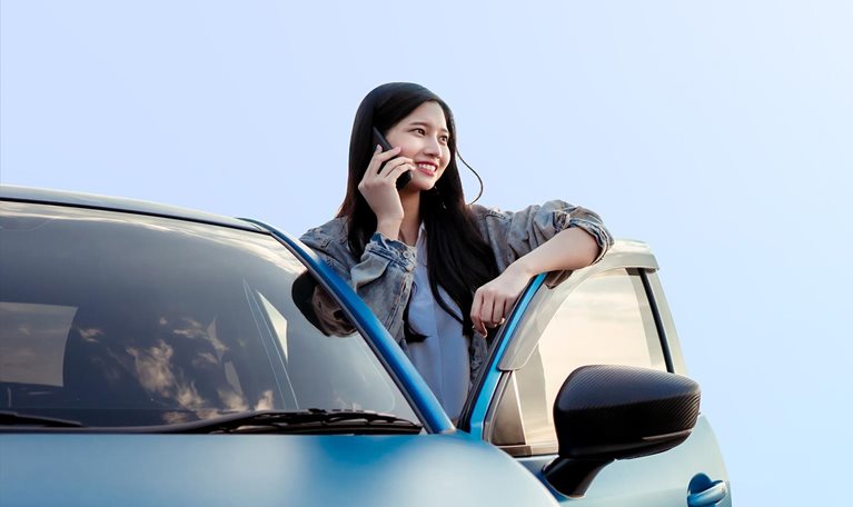 This image shows a person leaning against a blue car while talking on a phone.