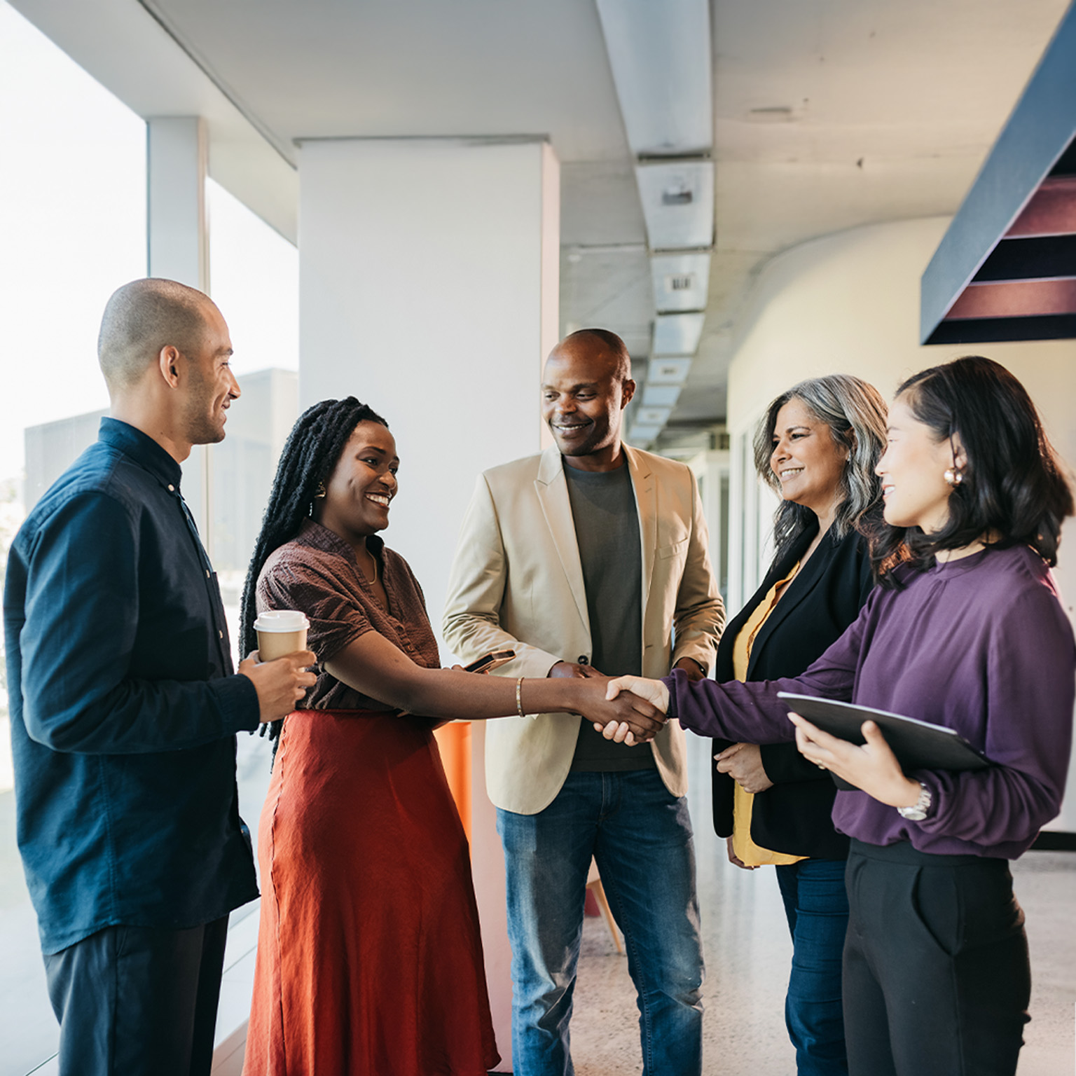 Multiracial group of business partners shaking hands, smiling and getting to know each other in coworking office space.