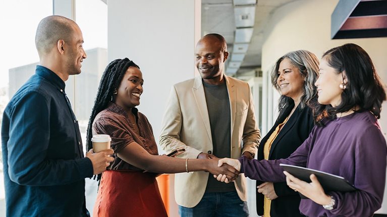 Multiracial group of business partners shaking hands, smiling and getting to know each other in coworking office space.
