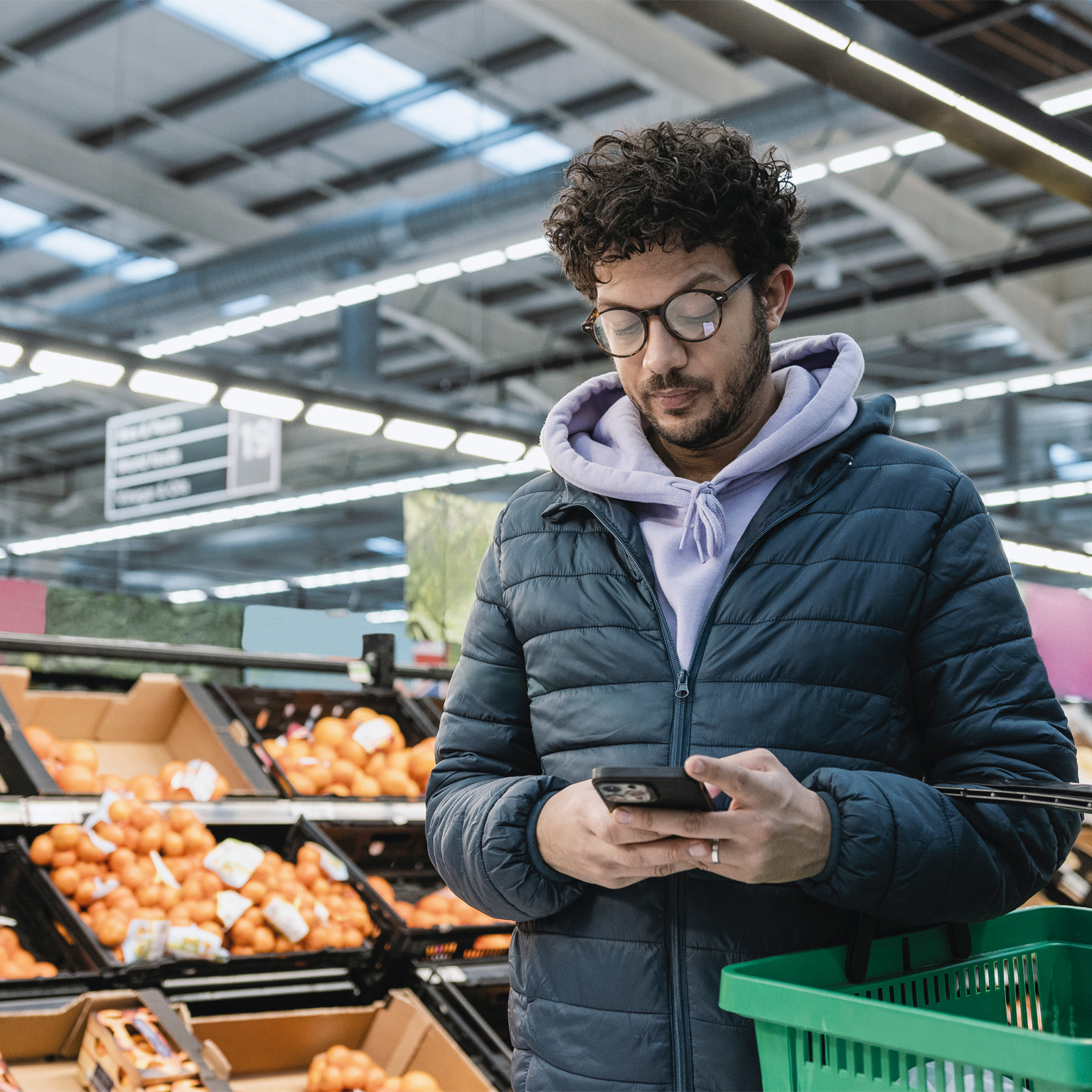 photo man in grocery store, holding shopping basket, looking at mobile phone