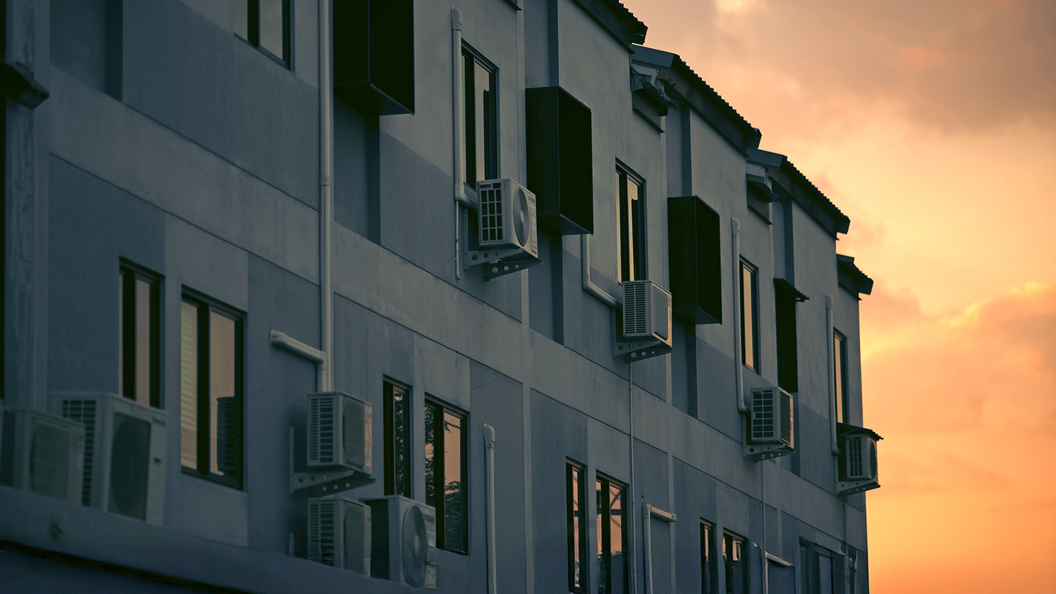 Image of an apartment building with air conditioning units next to the windows bathed in golden sunset.