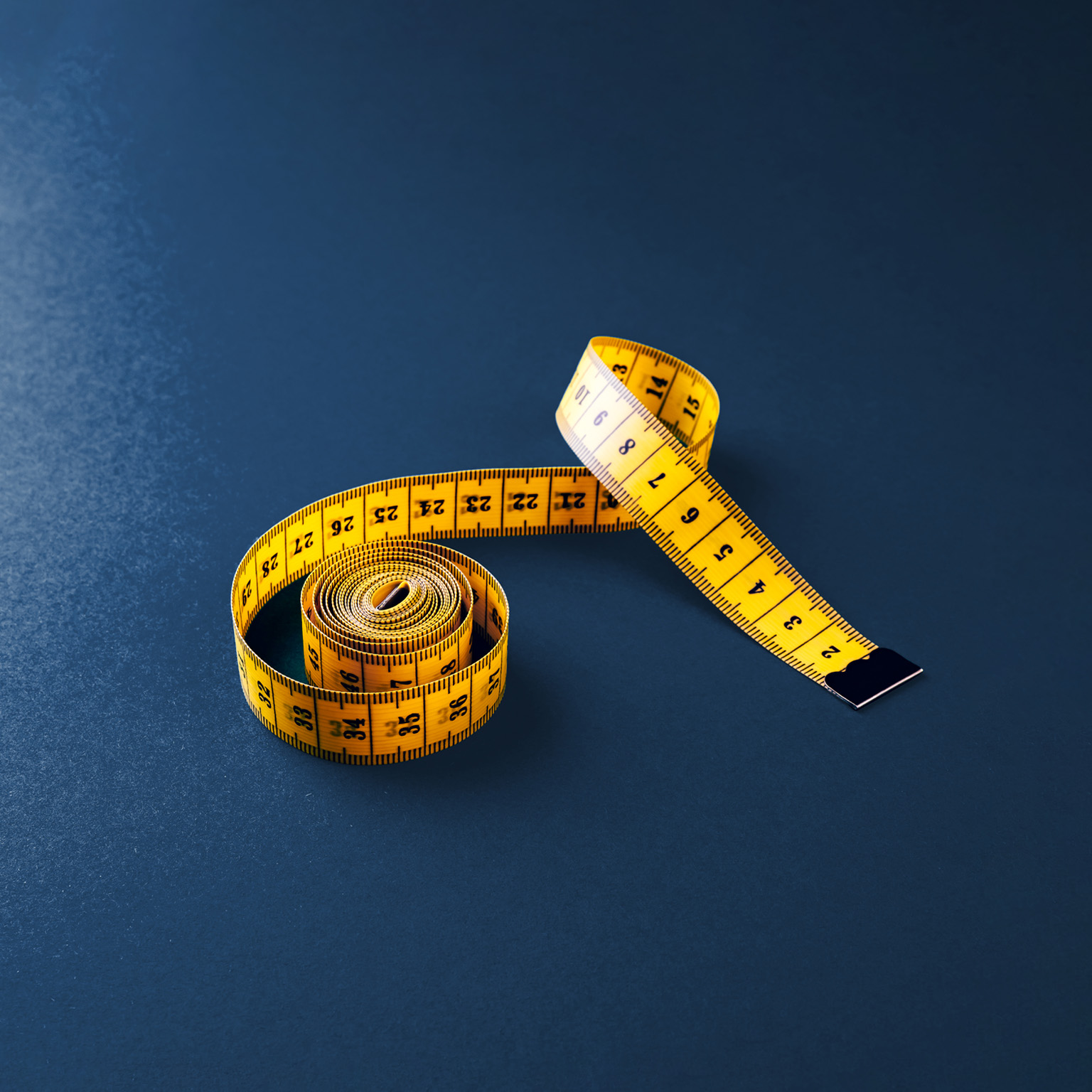 Yellow tailor's tape measure on a dark blue board.