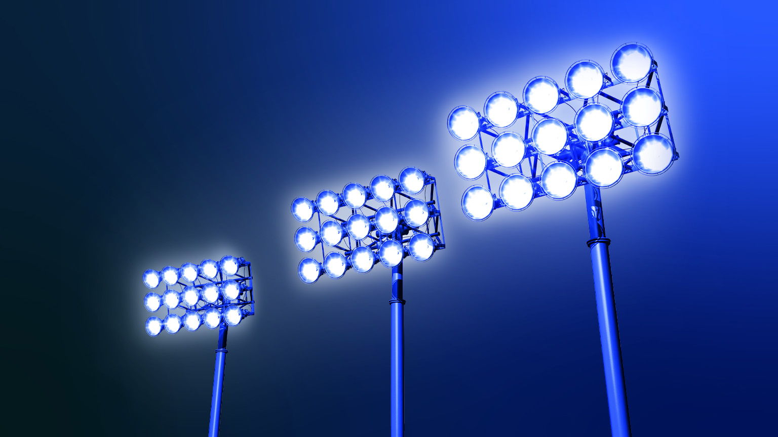 Against a dark blue backdrop, three sets of stadium lights emit a radiant glow, evoking a feeling of excitement and suspense.